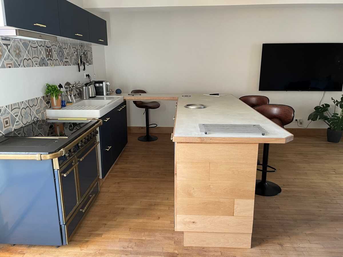 A modern kitchen with a built-in stove, a wooden island, bar stools, and a flat-screen TV mounted on the wall.