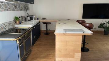 A modern kitchen with a built-in stove, a wooden island, bar stools, and a flat-screen TV mounted on the wall.
