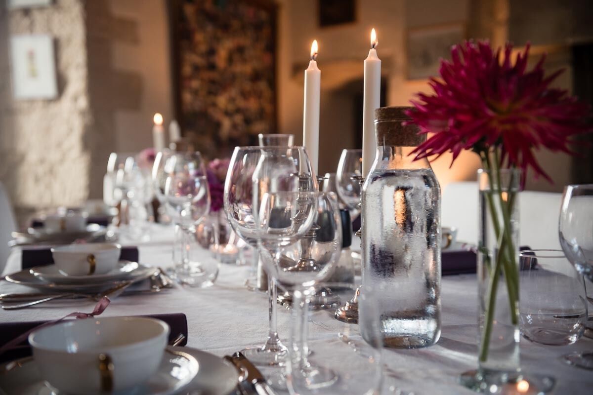 A table set for dining with clear glassware, candles, and a vase with a flower.