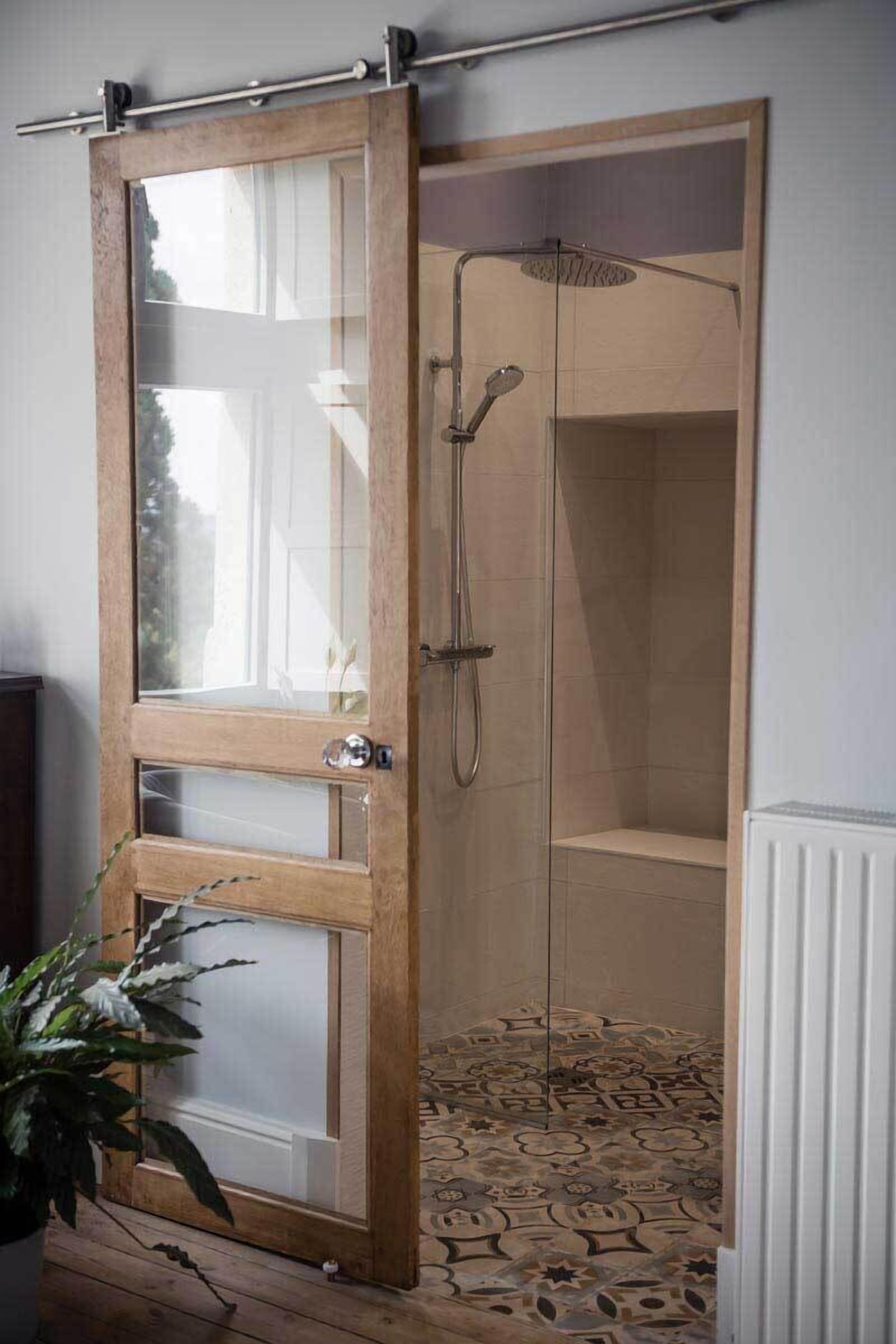A wooden door with glass panels leading to a shower area with a patterned floor.