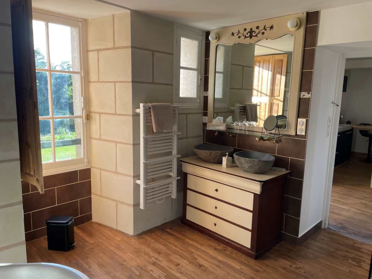 A bathroom with a wooden floor, a white towel rack, a beige vanity with two sinks, and a large mirror.