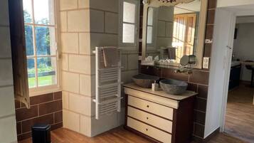 A bathroom with a wooden floor, a white towel rack, a beige vanity with two sinks, and a large mirror.