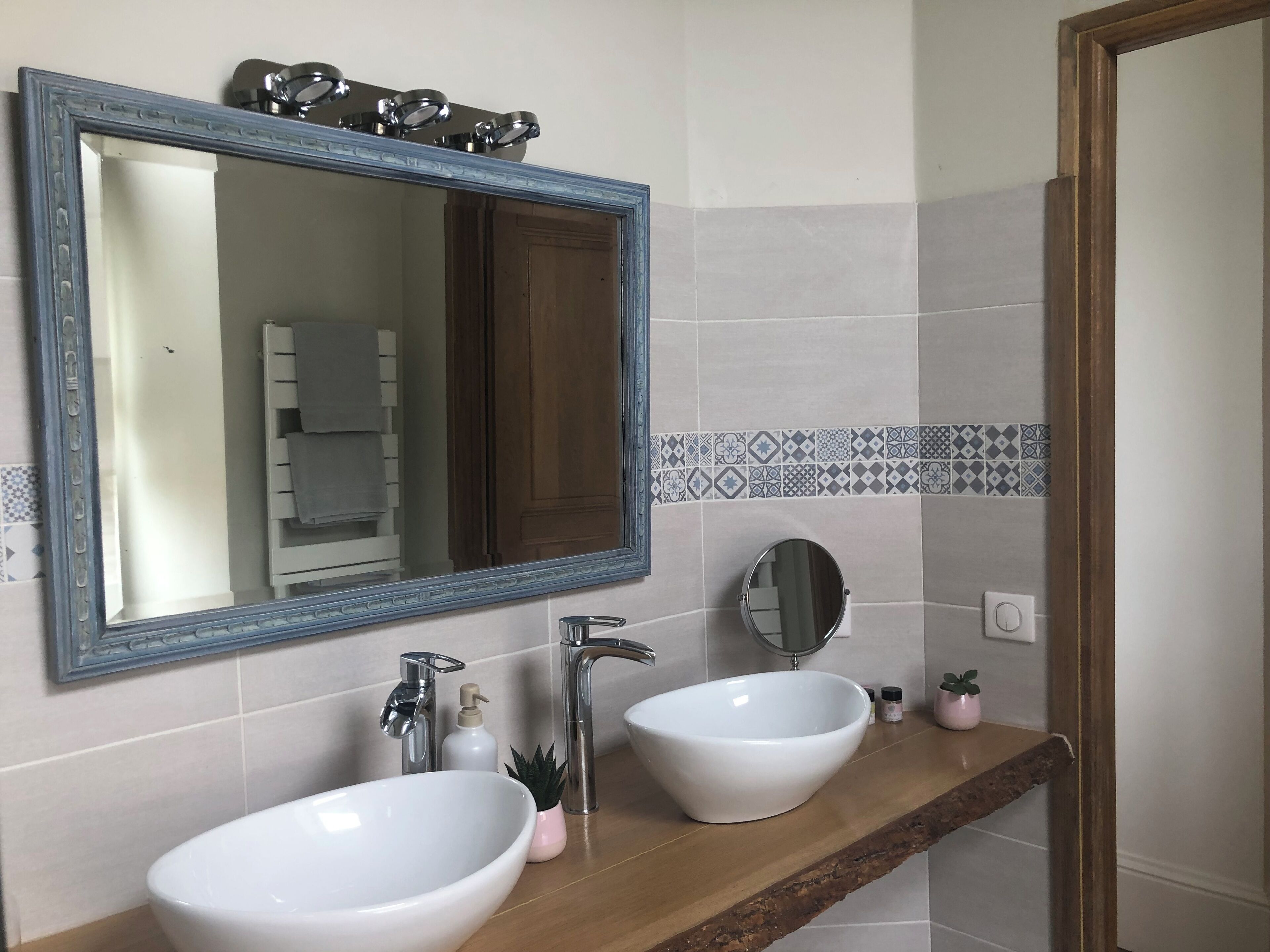 A bathroom with two white sinks, a large mirror, and a wooden shelf.