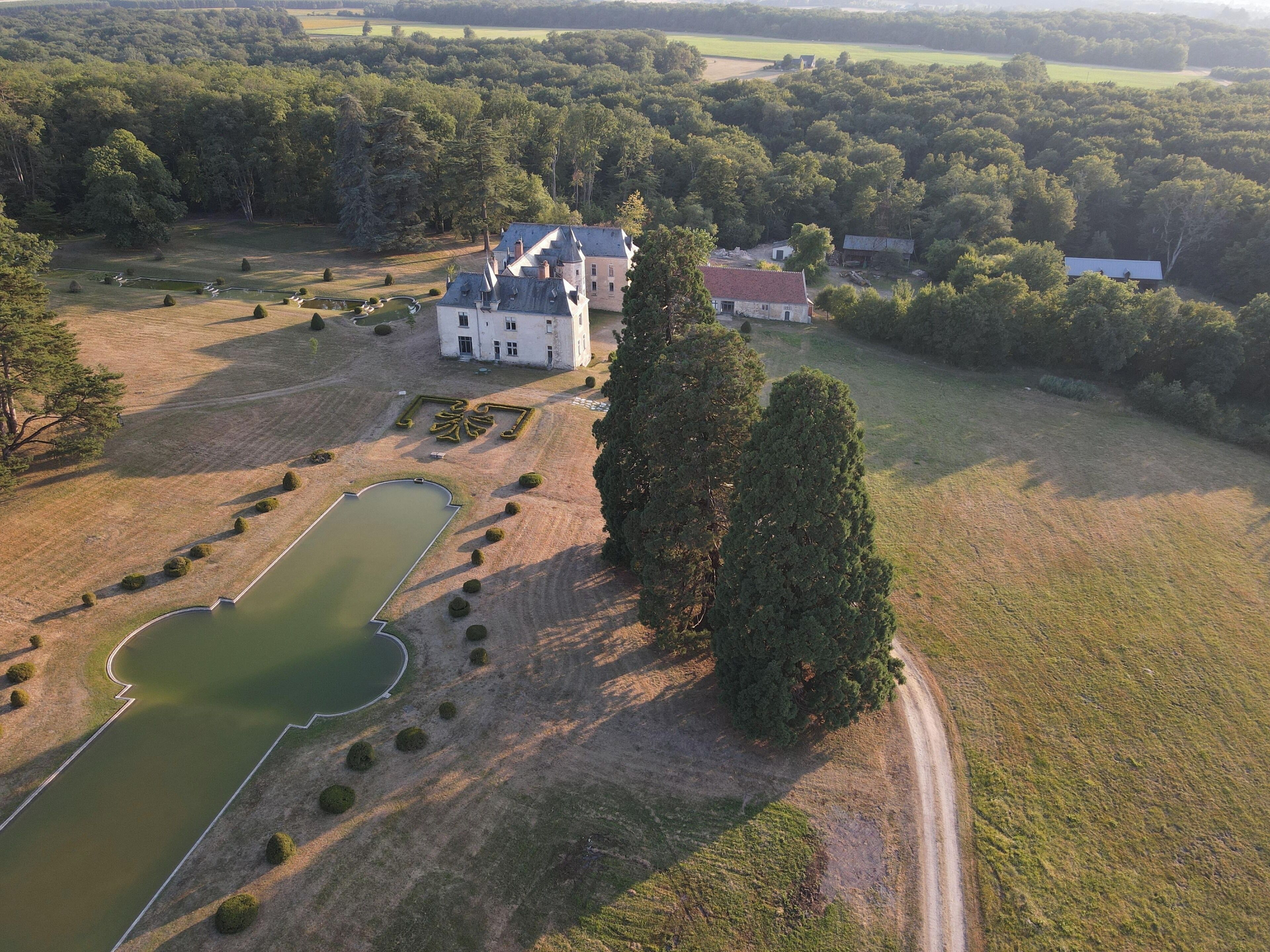 An aerial view of a large estate with a main building, a pond, and a well-maintained garden.