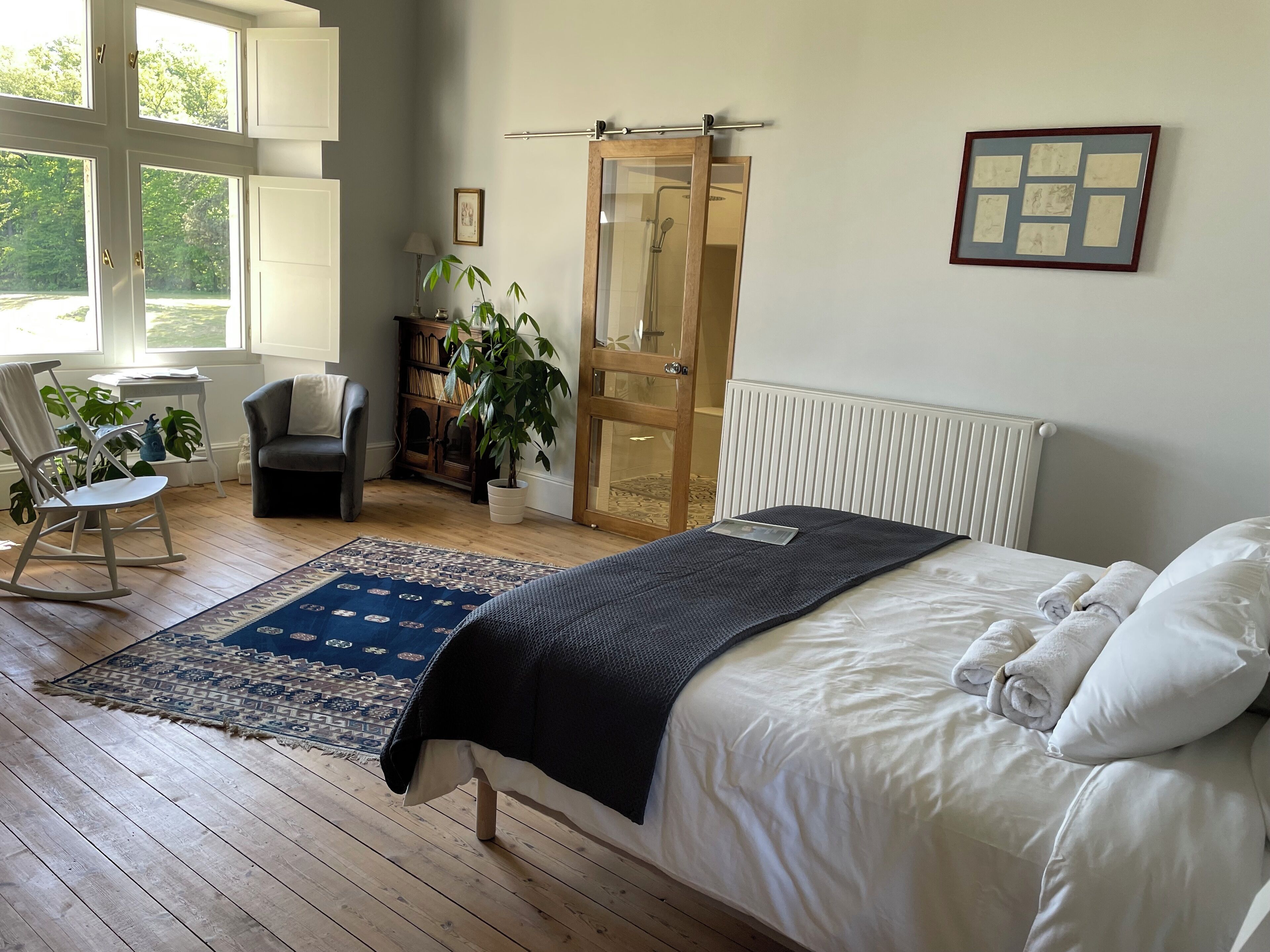 Ein Schlafzimmer mit Bett, Stuhl, Schreibtisch, Pflanze und Fenster.