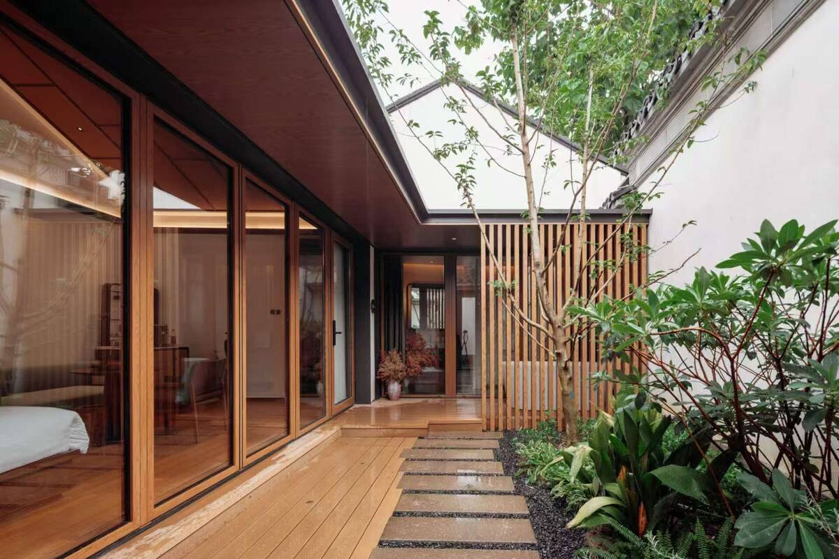 Une maison moderne dotée de grandes portes vitrées, d’une terrasse en bois et d’une variété de plantes.