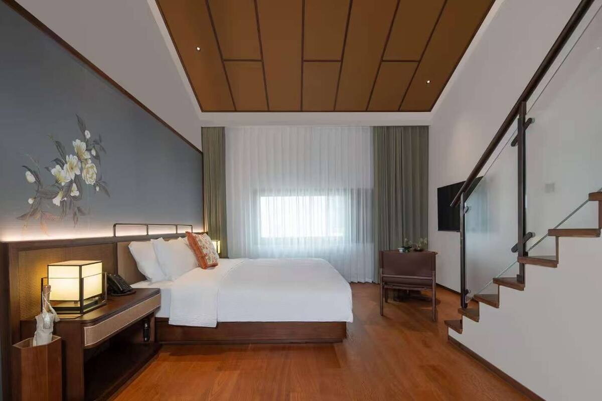 Une chambre d’hôtel moderne avec un grand lit, une table de chevet avec une lampe, un petit bureau et un escalier.