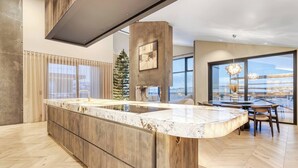 Una cucina moderna con un piano di lavoro in marmo, mobili in legno e una grande isola. C'è un'area pranzo con tavolo e sedie, e un'ampia finestra con vista sulla città.