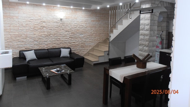 A modern living room with a stone wall, a black leather sofa, a coffee table, and a staircase leading to an upper level. - comfortable family-sized apartment for 4 people Ines 2 (Pula)