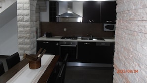 A modern kitchen with a stone accent wall, built-in appliances, and a dining area with a table and chairs. - comfortable family-sized apartment for 4 people Ines 2 (Pula)