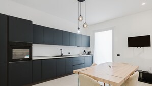 Una cucina moderna con mobili scuri, un tavolo da pranzo in legno e una TV a schermo piatto montata a parete.