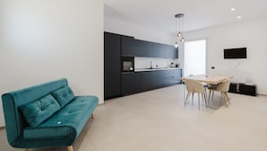 Una cucina moderna con mobili scuri, un tavolo da pranzo con sedie e un divano color petrolio.