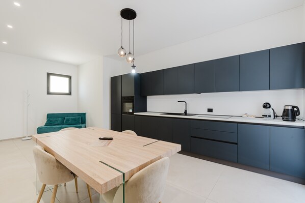 A modern kitchen with dark cabinets, a wooden dining table, and a teal sofa.