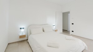 A modern bedroom with a large bed, bedside lamps, and a door leading to another room. - GC Luxury Apartments & Spa 'Deluxe Apartment' with Wi-Fi and Air Conditioning (Santa Margherita di Belice)