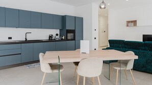A modern kitchen with blue cabinets, a wooden dining table, and a teal sofa. - GC Luxury Apartments & Spa 'Deluxe Apartment' with Wi-Fi and Air Conditioning (Santa Margherita di Belice)