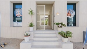 A building entrance with a set of steps leading up to a door, flanked by potted plants and two large windows with university branding. - GC Luxury Apartments & Spa 'Deluxe Apartment' with Wi-Fi and Air Conditioning (Santa Margherita di Belice)