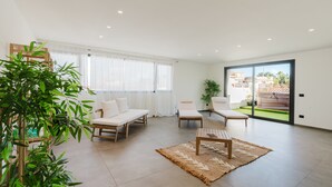 Amplia sala de estar con un gran ventanal corredero que da a un balcón, una mesa de centro de madera y un sofá.
