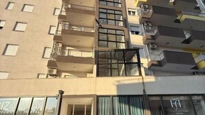 Un immeuble à plusieurs étages doté d’un escalier central, de balcons et d’une entrée au niveau du sol, avec une voiture garée à l’extérieur.