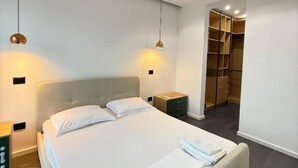 Une chambre moderne avec un grand lit, deux tables de chevet et un dressing.