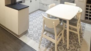 Une cuisine moderne avec des meubles blancs, un four encastré et un coin repas comprenant une table et des chaises blanches.