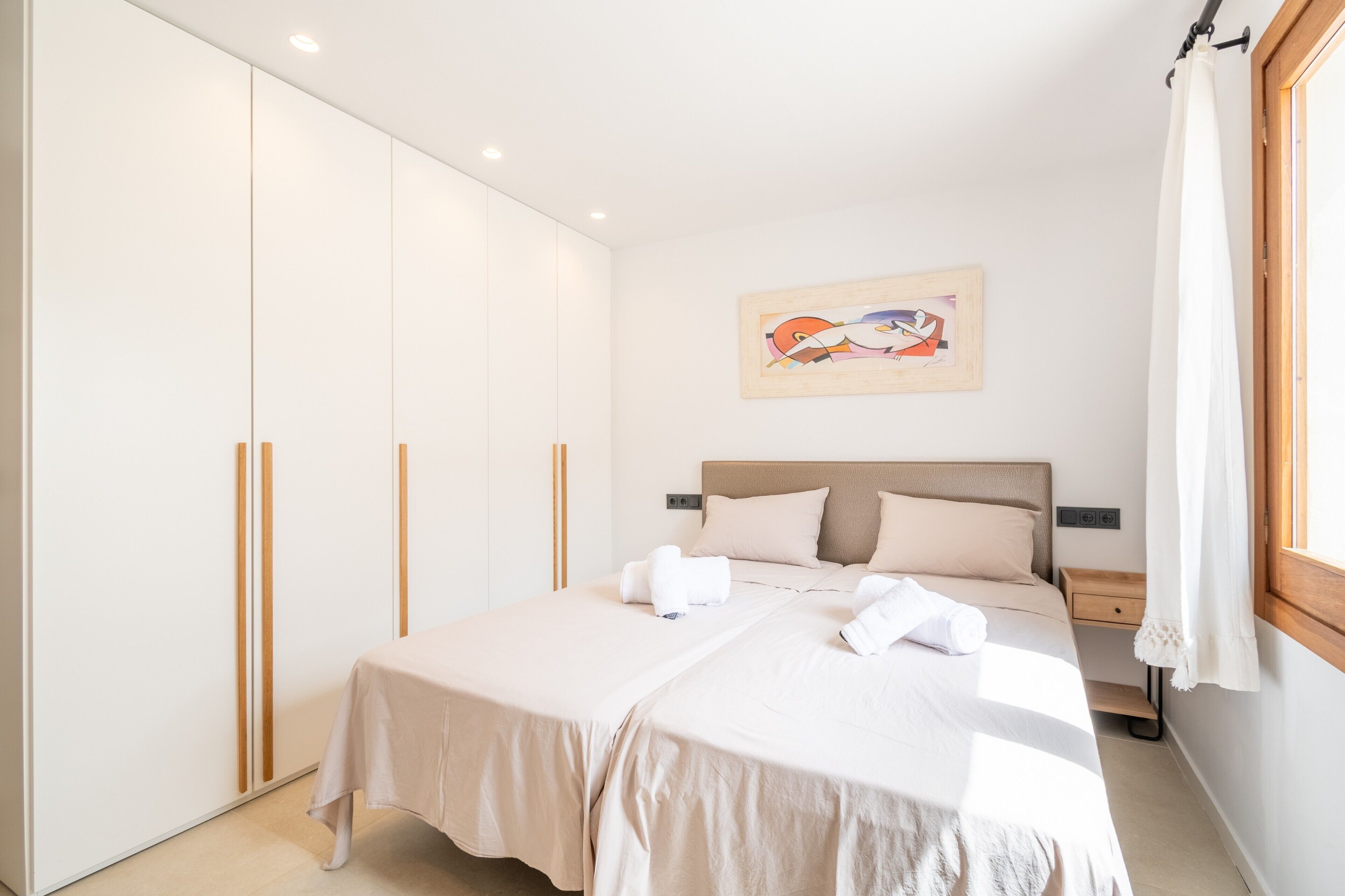 A hotel room with a bed, a wardrobe, a painting, and a window with curtains.
