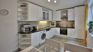 A compact kitchen with white cabinets, a microwave, a washing machine, and a sink. - Ostsee Domizil, App. 1 (Timmendorfer Strand)