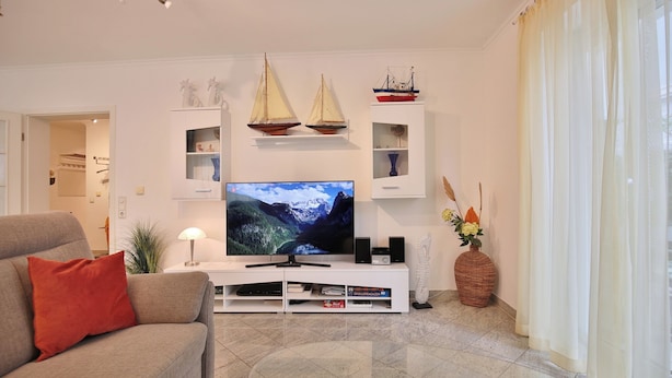A living room with a flat-screen TV, a sofa, a coffee table, and decorative items including model ships and a vase. - Ostsee Domizil, App. 1 (Timmendorfer Strand)