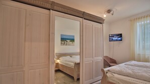A bedroom with a wooden bed, a TV mounted on the wall, and a sliding closet door. - Ostsee Domizil, App. 1 (Timmendorfer Strand)