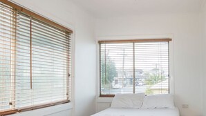 A bedroom with a bed, a ceiling fan, and two windows with blinds. - The Happy Pelican Harrington Hotel (Harrington)