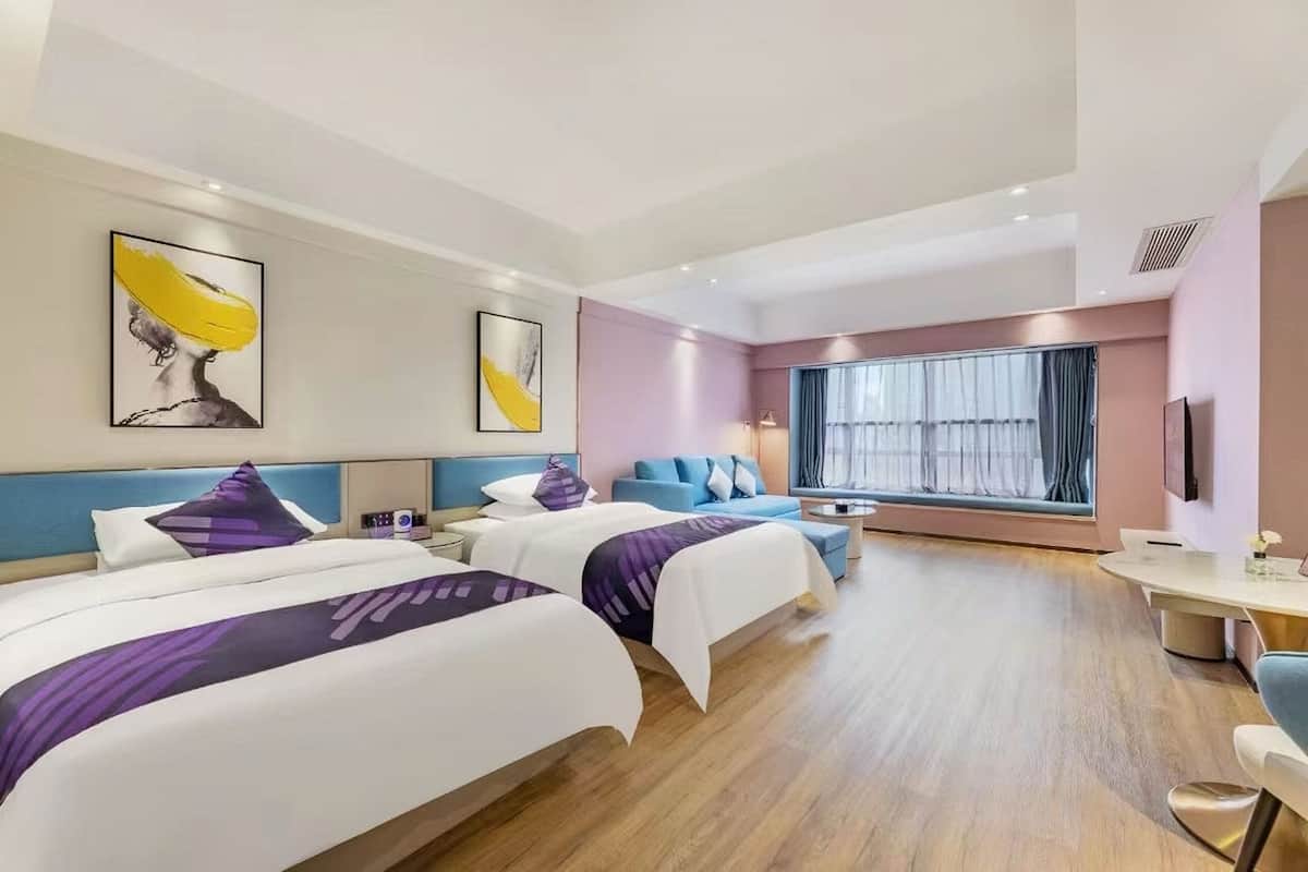 Ein Hotelzimmer mit zwei Betten, einem Schlafsofa, einem Schreibtisch und einem großen Fenster mit Vorhängen.