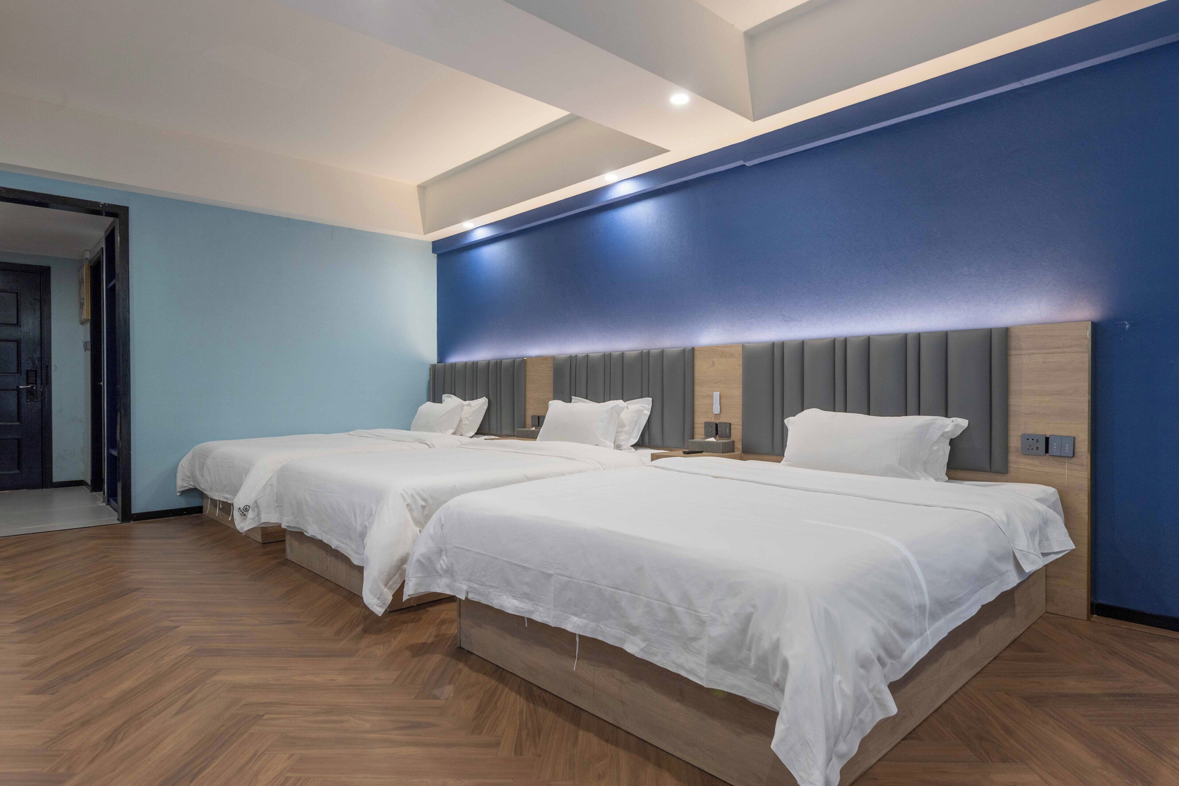 Habitación de hotel con dos camas, suelo de madera y una pared azul.
