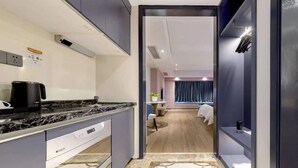 A modern hotel room with a kitchen area, a bed with a blue curtain, and a small seating area. - Pazhou Poya International Hotel Canton Fair Complex Modiesha Metro Exit B Branch - Free Shuttle Bus to Canton Fair Complex During Canton Fair Period (Guangzhou)