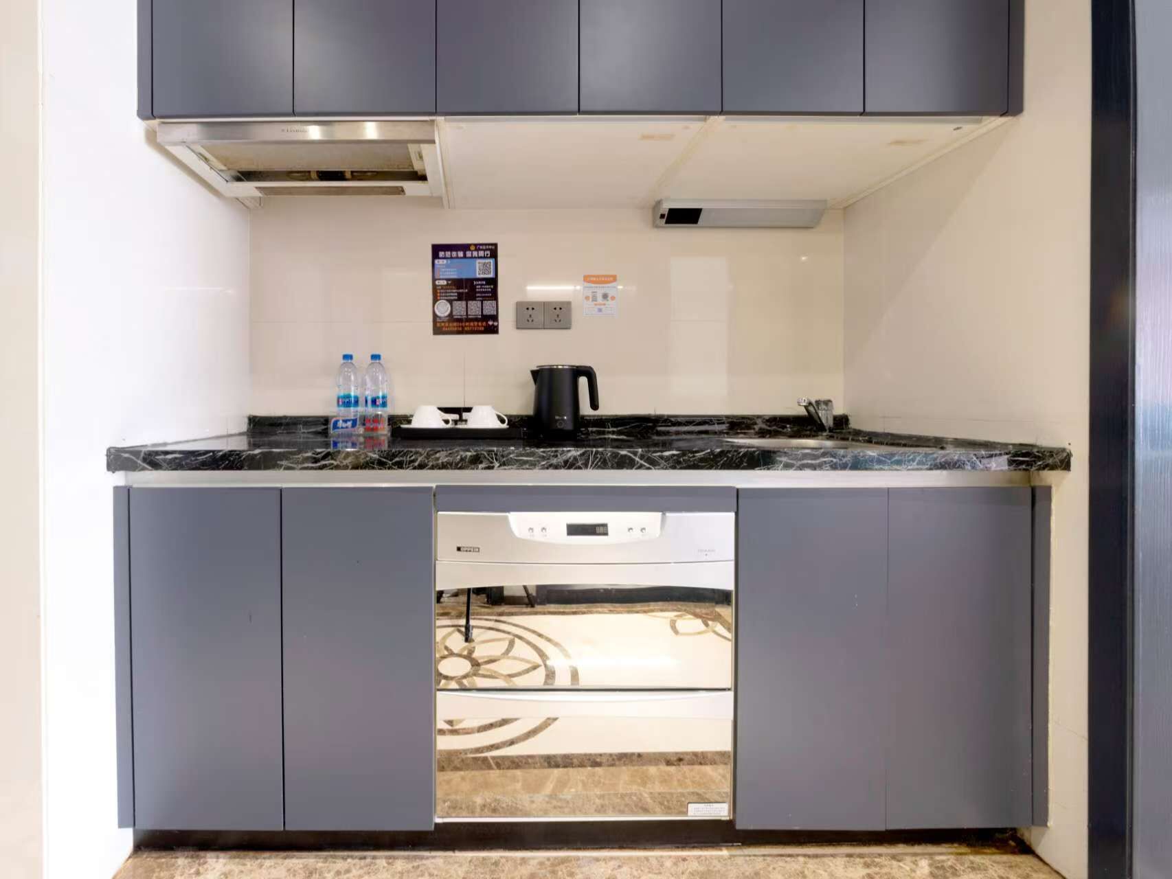 A compact kitchen with grey cabinets, a black marble countertop, and a built-in dishwasher.