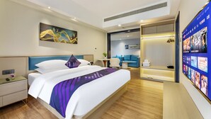 A modern hotel room with a large bed, a bedside table, a nightstand, a wall-mounted TV, and a sliding door leading to a seating area with a blue sofa and a small table. - Pazhou Poya International Hotel Canton Fair Complex Modiesha Metro Exit B Branch - Free Shuttle Bus to Canton Fair Complex During Canton Fair Period (Guangzhou)