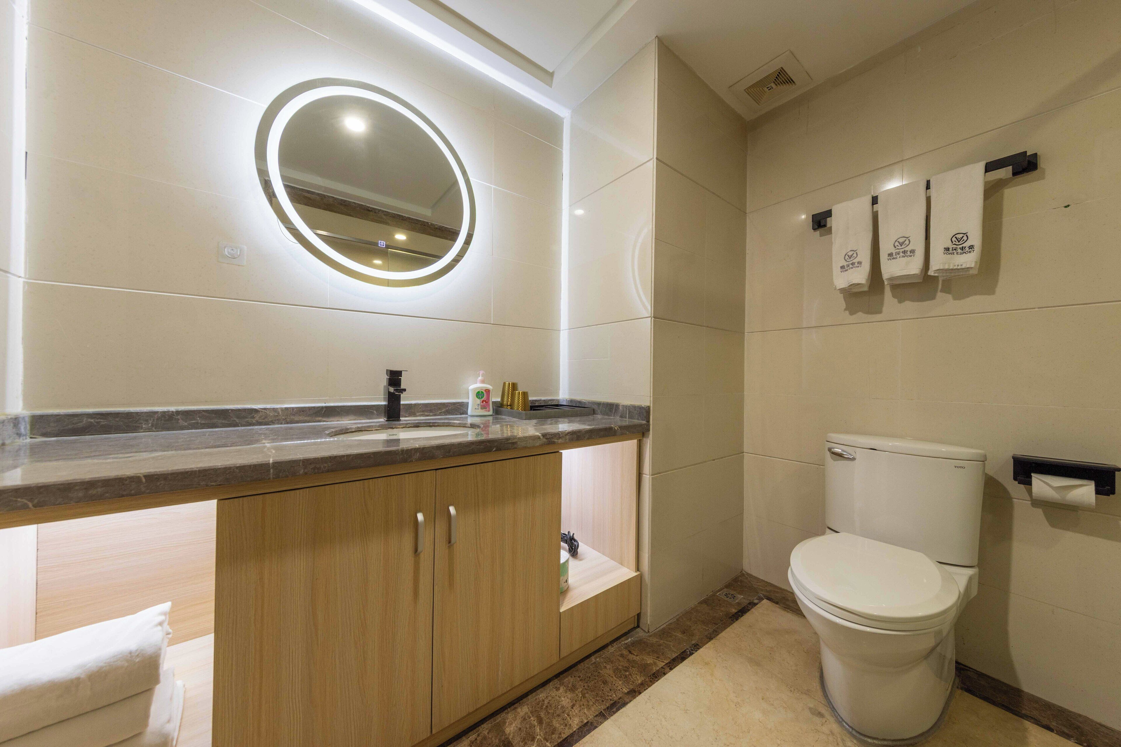 A modern bathroom with a marble countertop, wooden cabinets, a white toilet, and a wall-mounted towel rack.