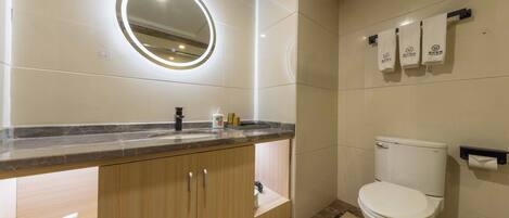 A modern bathroom with a marble countertop, wooden cabinets, a white toilet, and a wall-mounted towel rack.