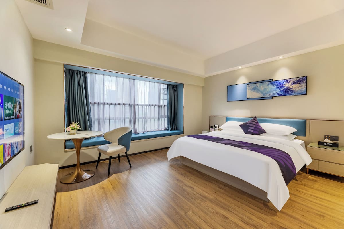 Ein modernes Hotelzimmer mit einem großen Bett, einem Schreibtisch, einem Stuhl und einem Fenster mit Vorhängen.