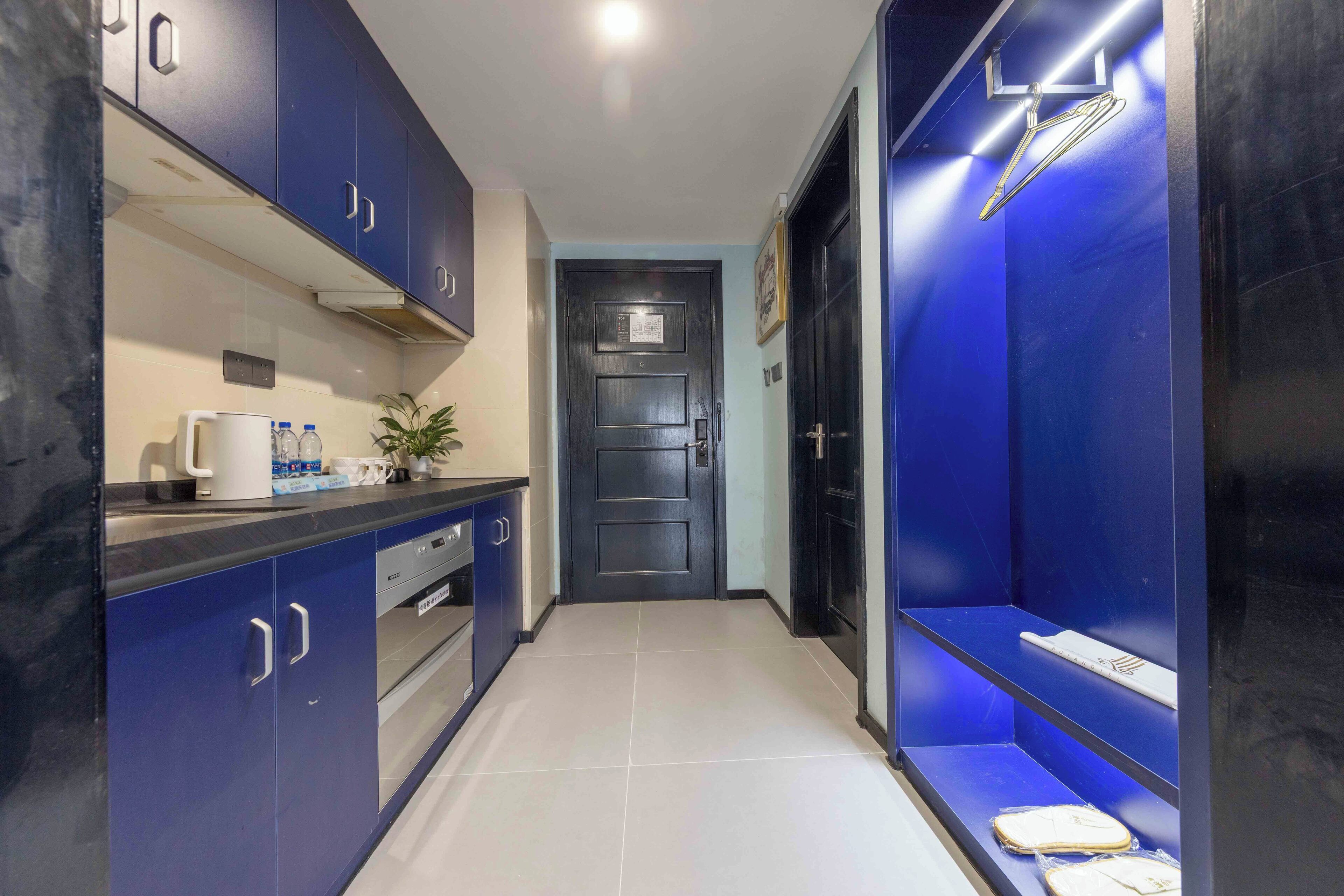 Un pasillo estrecho con armarios azules, una encimera blanca con una cafetera y una puerta con un aviso.