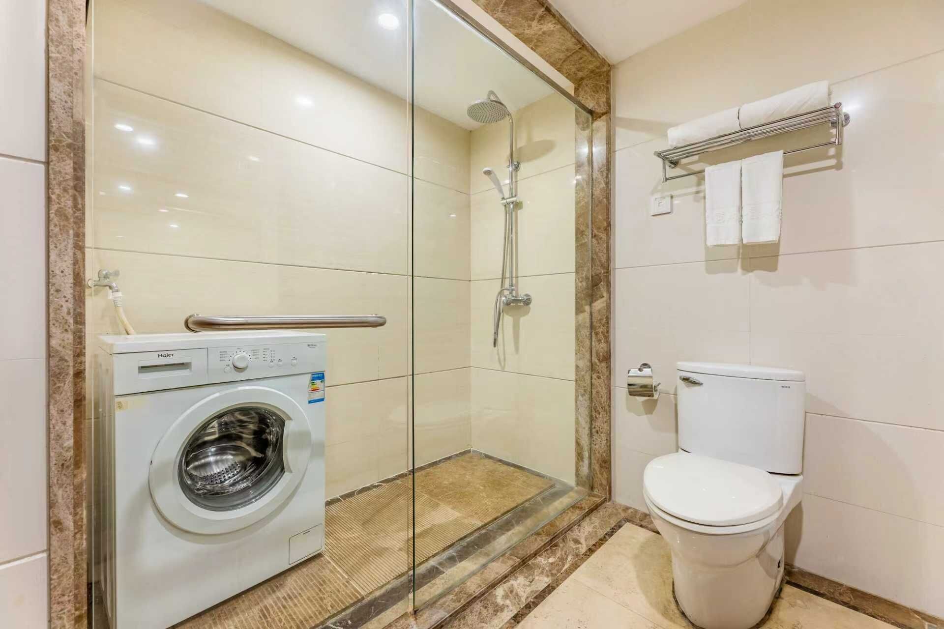 A compact bathroom with a glass-enclosed shower, a built-in washing machine, and a toilet.