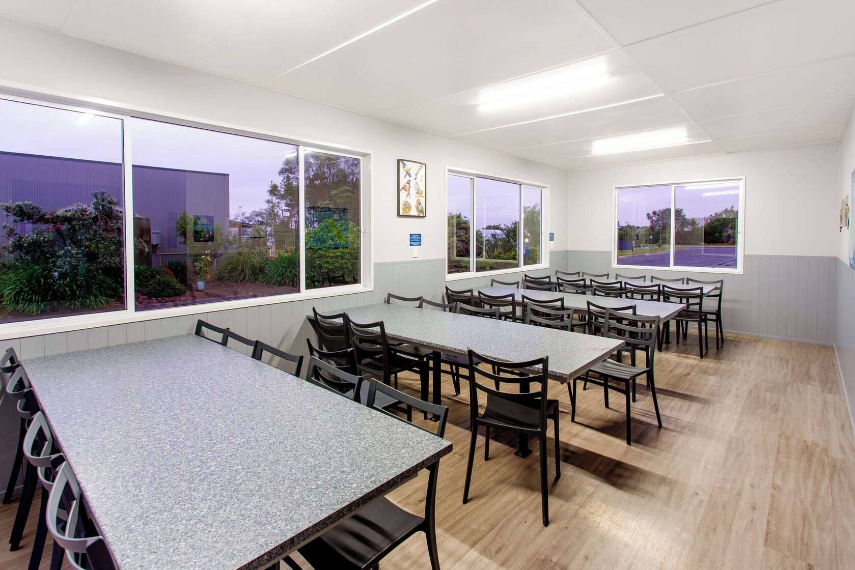 A conference room with multiple tables and chairs, large windows with views of greenery, and a clean, modern design.