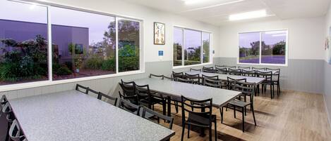 A conference room with multiple tables and chairs, large windows with views of greenery, and a clean, modern design.