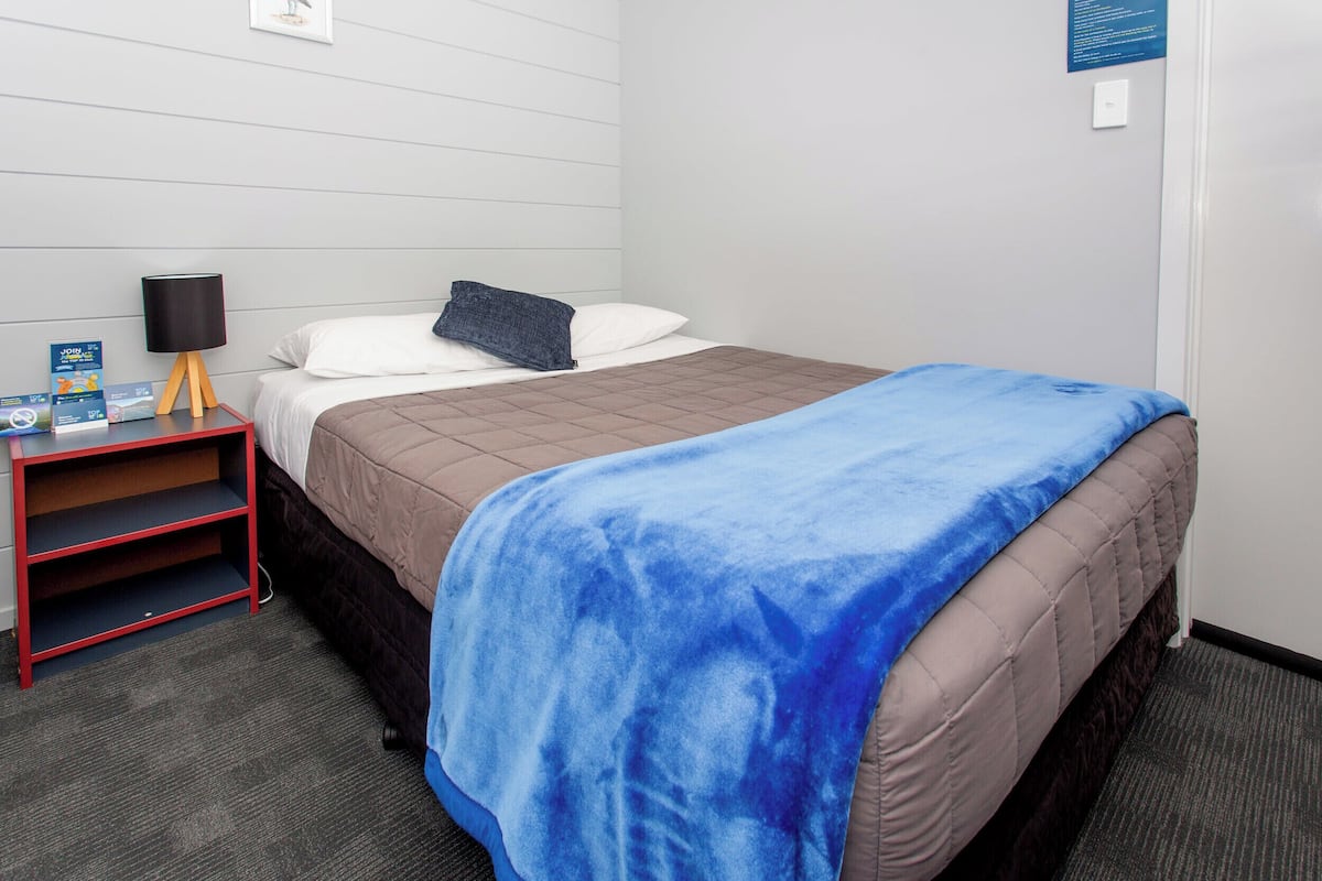 Una habitación de hotel con cama, mesita de noche, lámpara y manta azul.