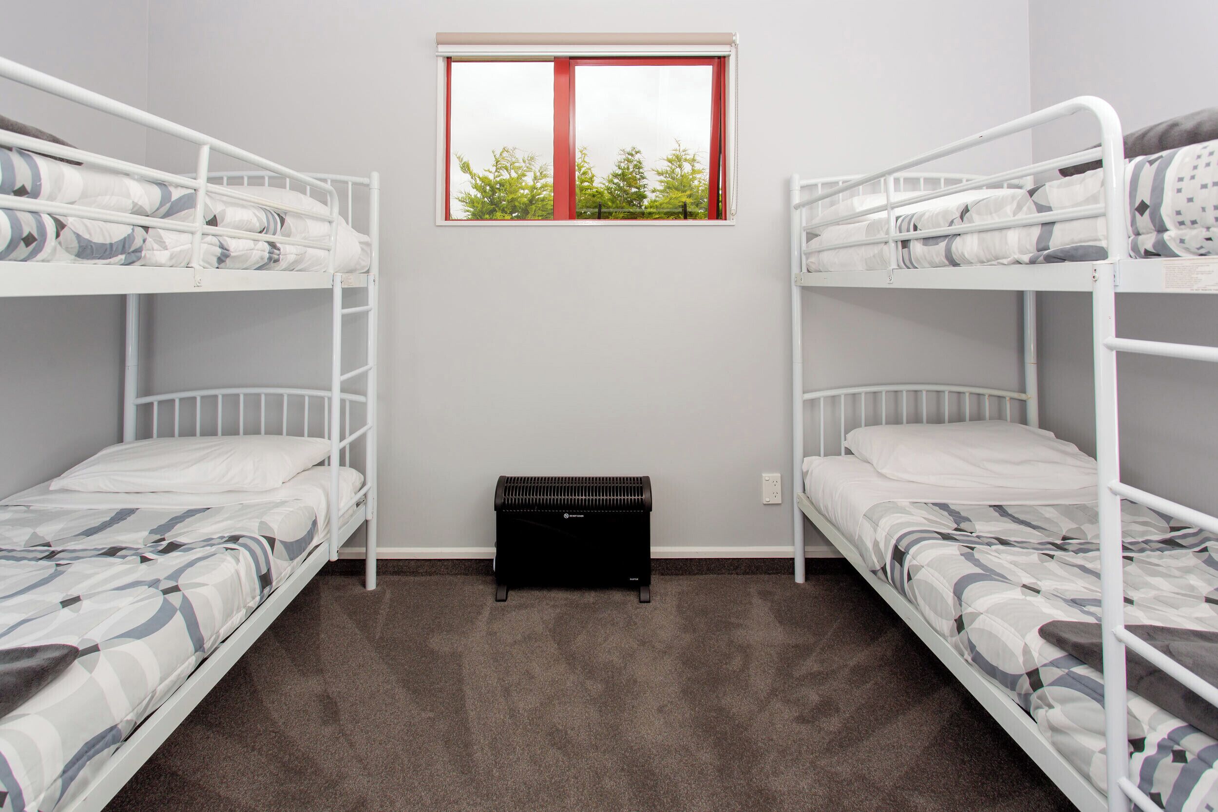 A room with two bunk beds, a small window with a red frame, and a black storage unit.