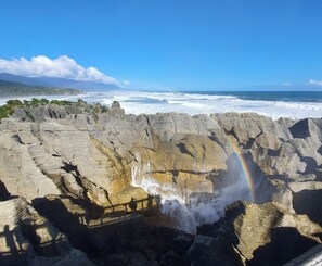 Un paisaje costero con una cascada, un arcoíris y vistas al océano y montañas distantes.