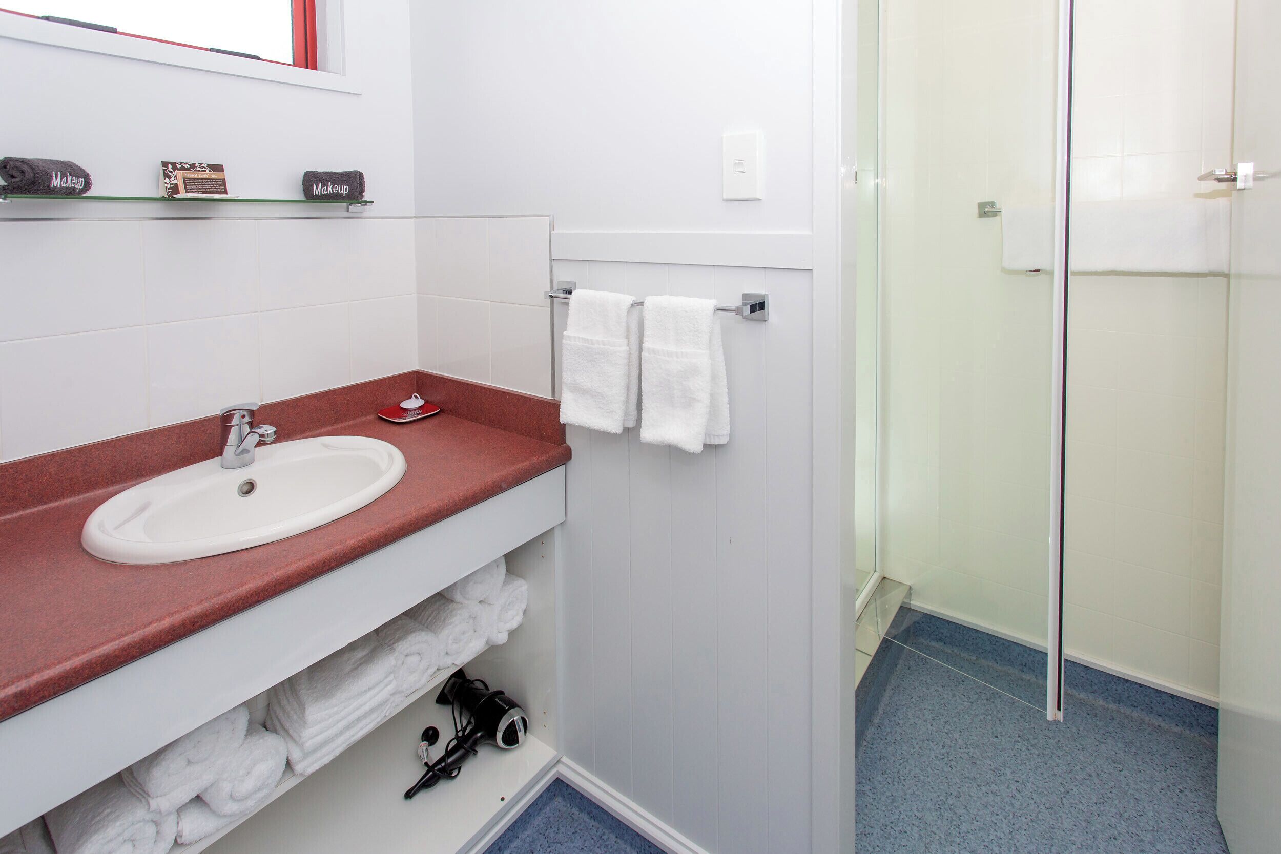 Een badkamer met een witte wastafel, een rode aanrecht en een douchecabine met glazen wanden.