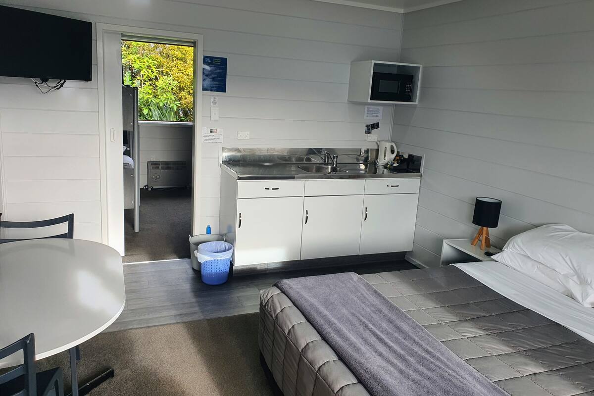 Habitación de hotel compacta con kitchenette, una cama, una mesita y una silla.