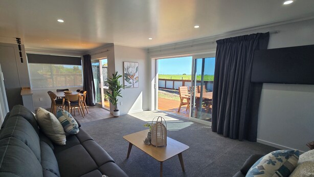A modern living room with a sofa, a coffee table, and a dining area with chairs and a table. - Carters Beach Top 10 Holiday Park (Westport)