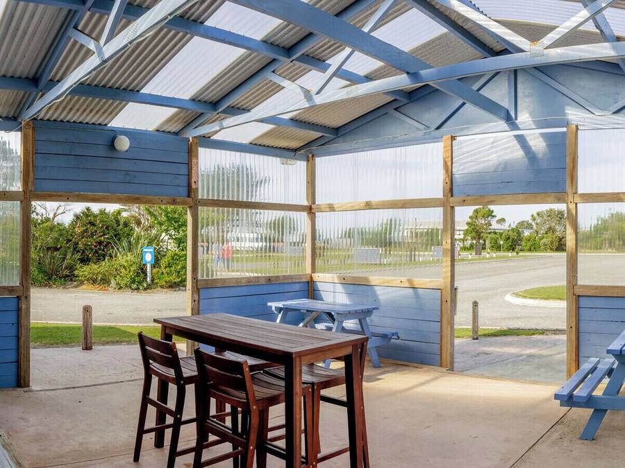 A covered patio area with a table and chairs, a grill, and a view of the street.