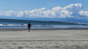 A person walking on a beach with a clear sky and distant mountains. - Carters Beach Top 10 Holiday Park (Westport)