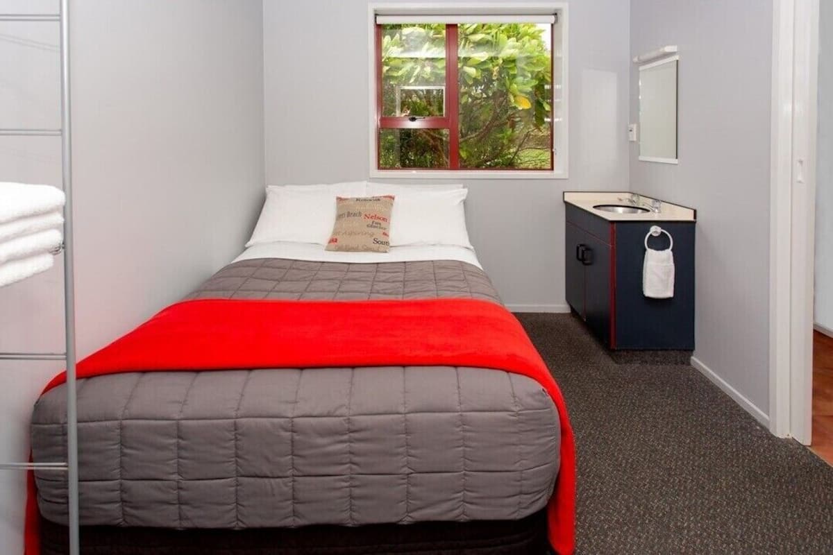 Un dormitorio con cama, ventana con vistas a la vegetación, mesita de noche con toalla y un mueble pequeño.